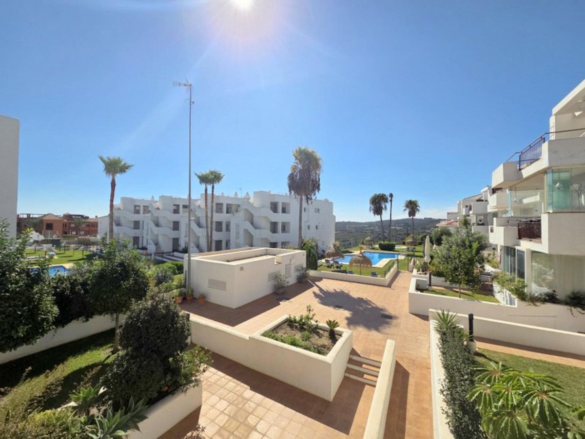 Resort complex with white buildings, palm trees, swimming pool, and green garden under a clear blue sky.