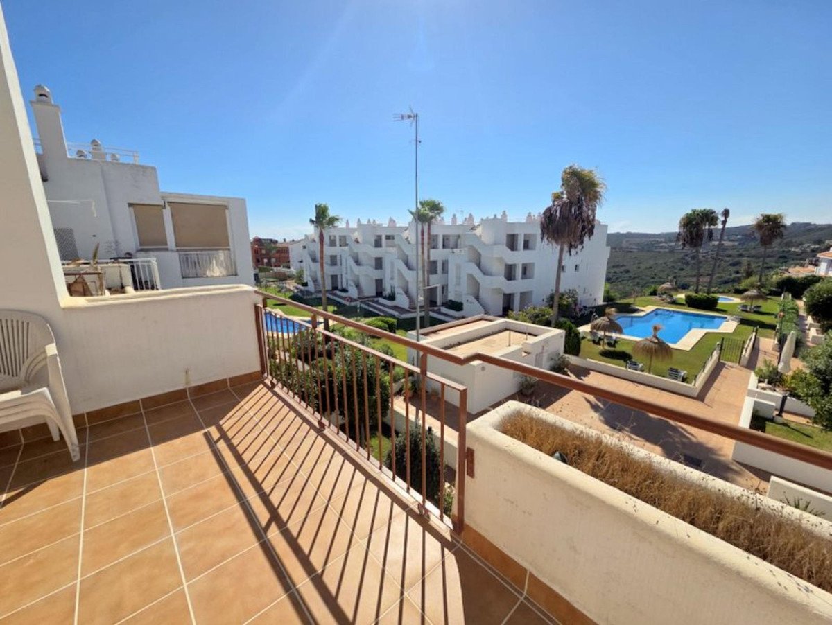 View from a balcony overlooking a swimming pool, gardens, and apartment buildings under a clear blue sky.