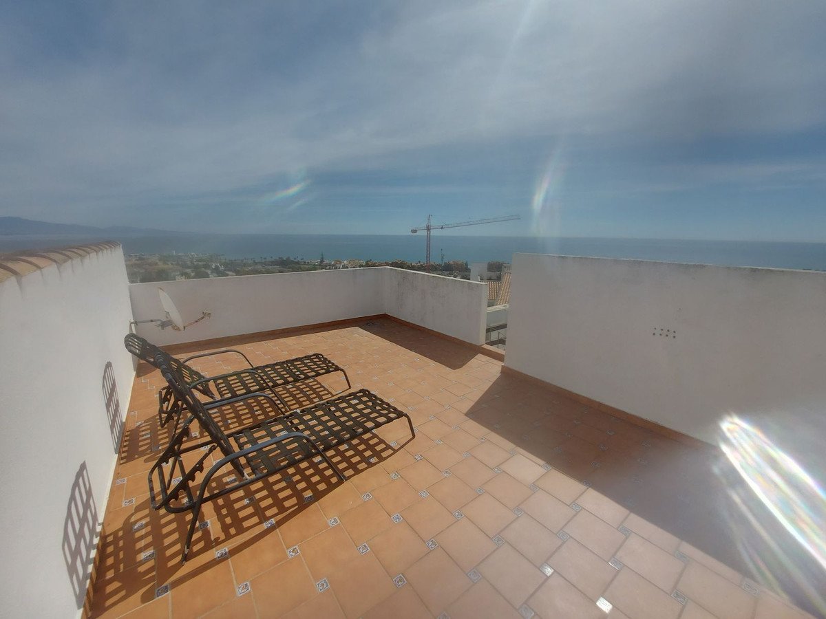 Terrace with two lounge chairs offering a panoramic sea view and distant cityscape. Sunny day with blue sky.