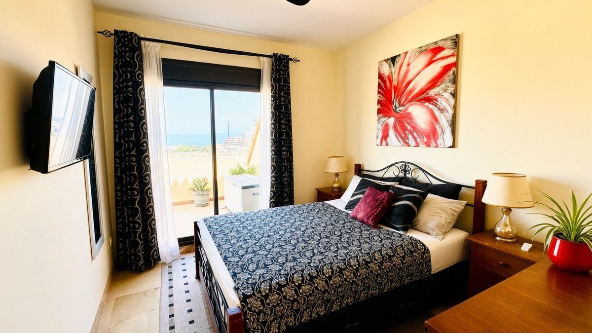 Bedroom with a large bed, a balcony with sea view, a TV on the wall, and floral artwork.