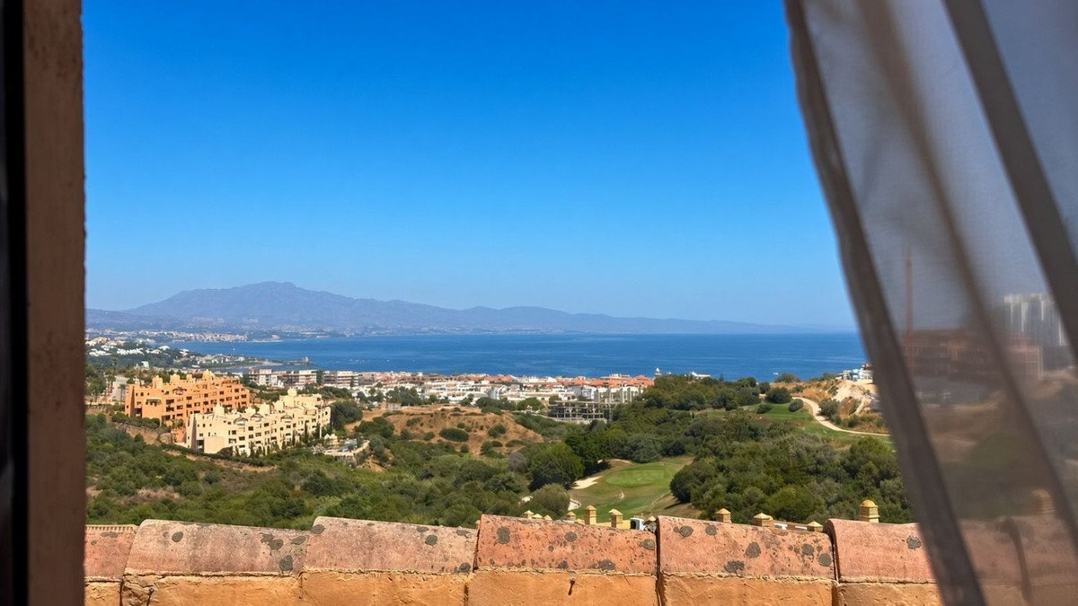View from window of a golf course and the sea with mountains in the background under a clear blue sky.