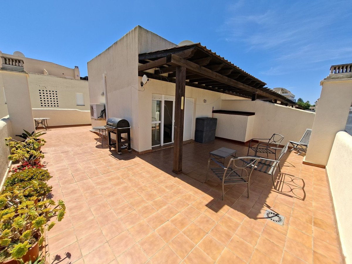 A spacious tiled terrace with a barbecue, seating area, and plants, featuring a wooden pergola and outdoor air conditioning unit.