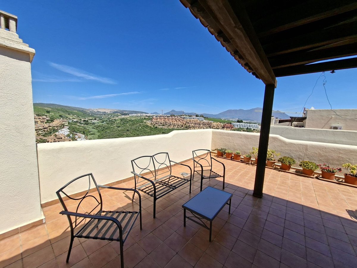 Spacious terrace with seating, potted plants, and a beautiful panoramic view of hills and mountains under a clear blue sky.
