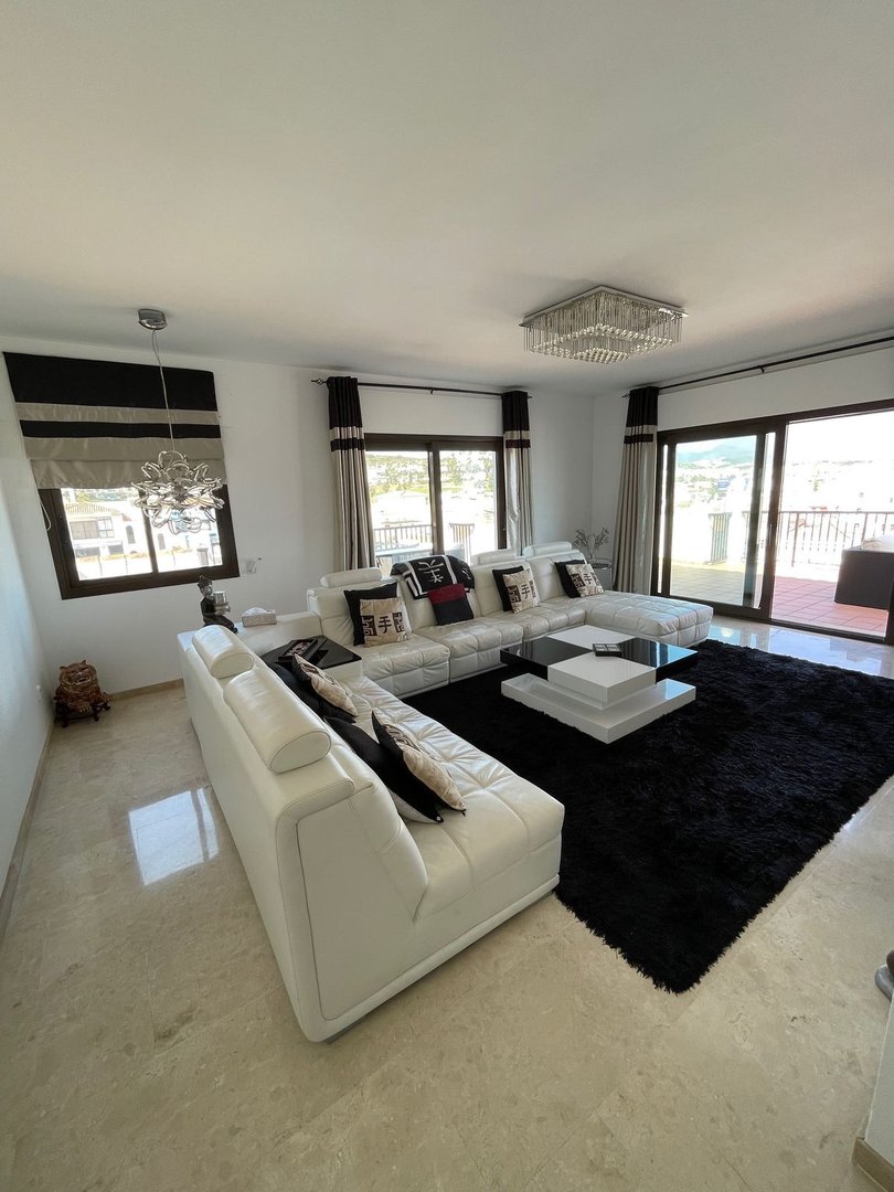 Modern living room with a large white sectional sofa, black rug, and balcony doors offering a distant view.