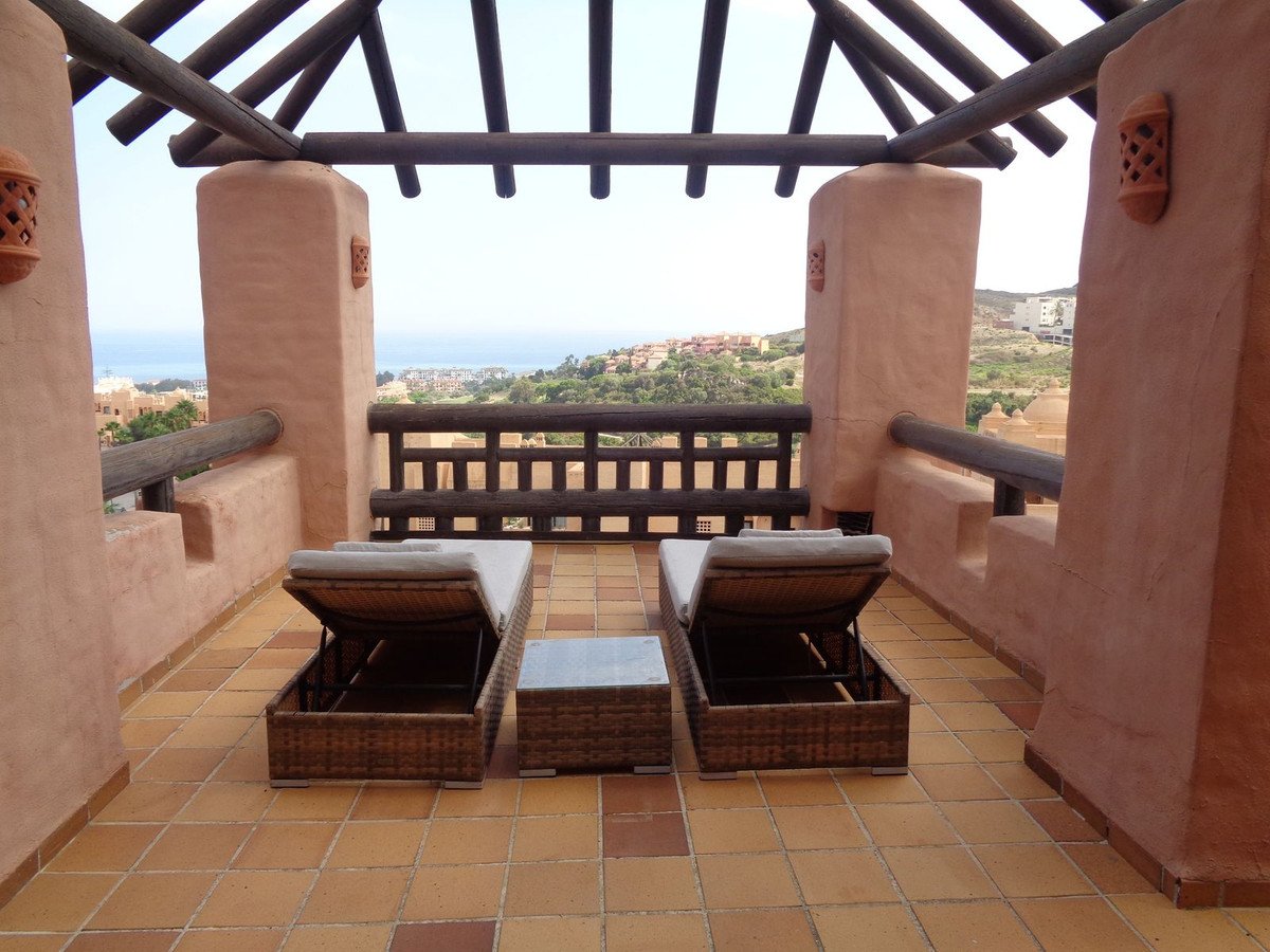 Terrace with lounge chairs and a small table overlooking the sea and distant buildings.