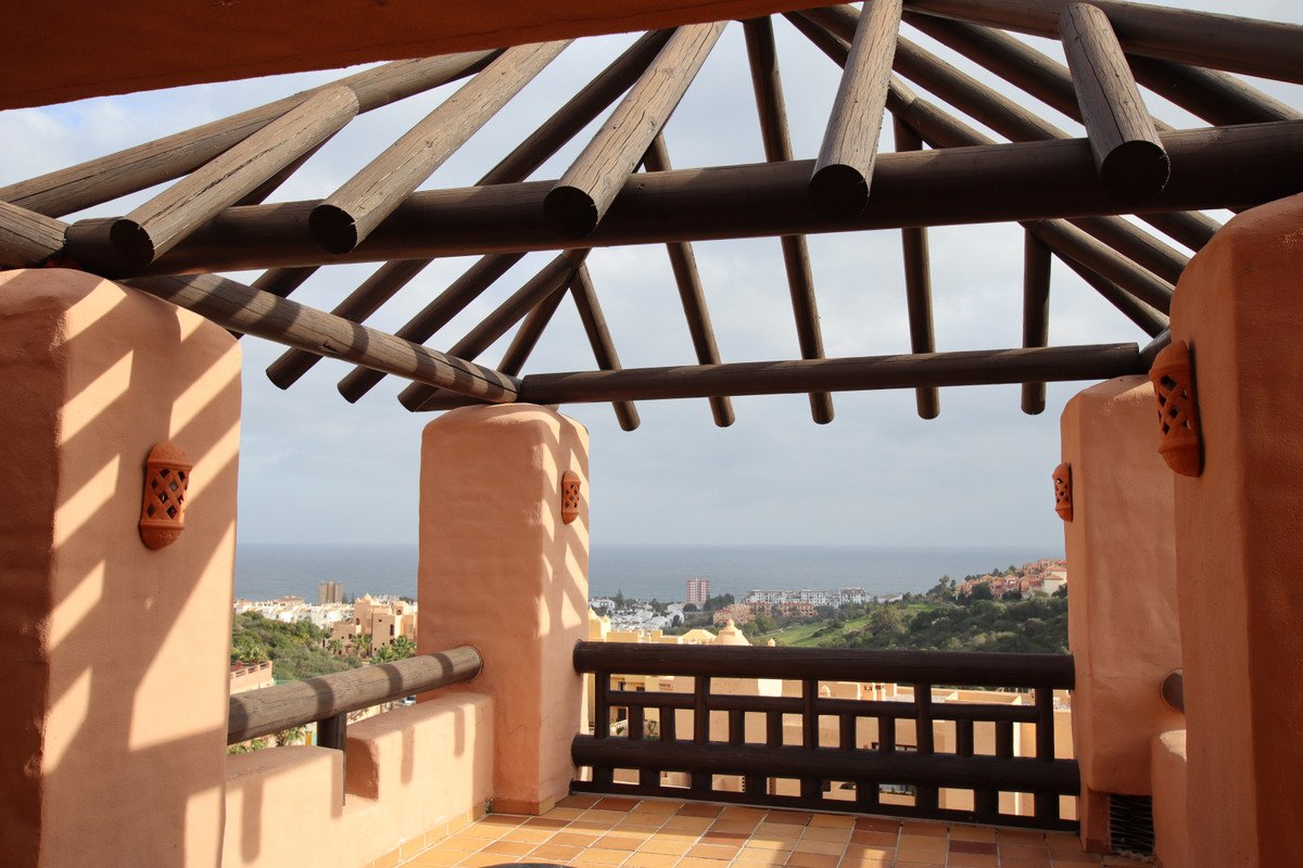Terrace with wooden beams and sea and village view. Balcony features terracotta accents and a wooden railing.