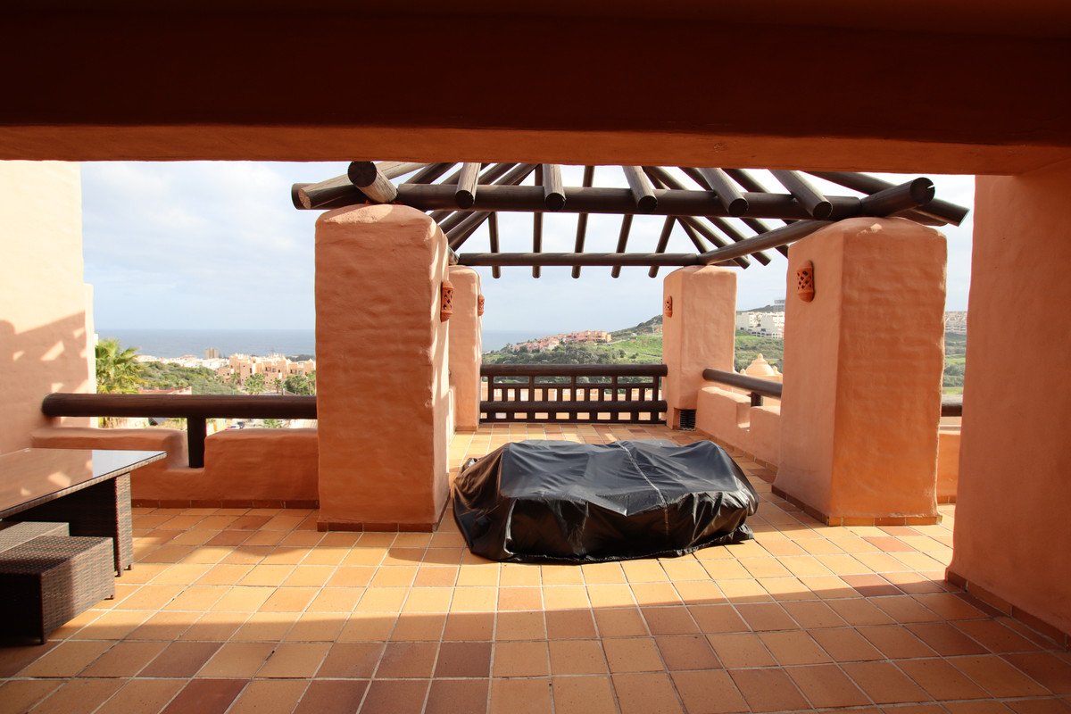 Terrace with a covered outdoor furniture, wooden pergola, and a view of the sea and distant town.