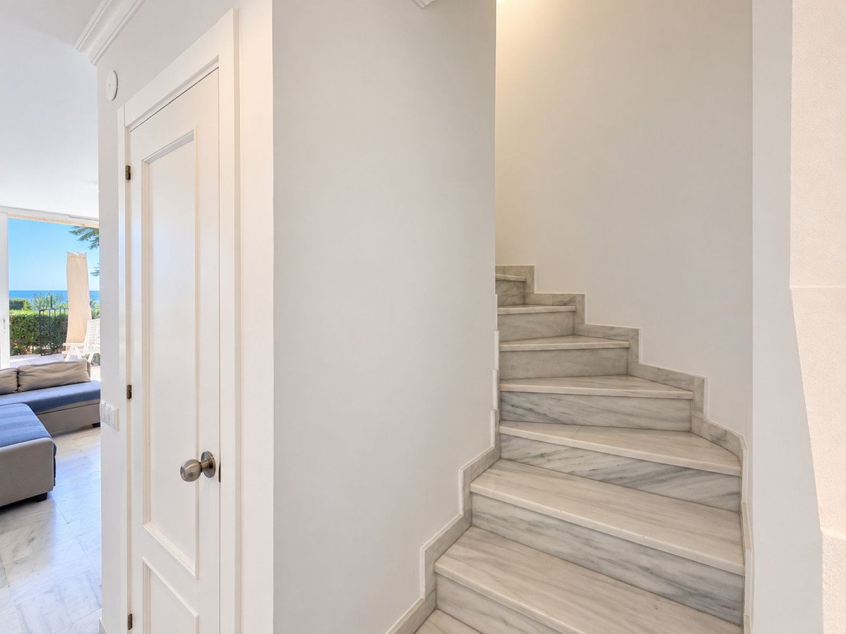 Interior view of marble stairs and a hallway with a door leading to an outdoor area with a glimpse of the ocean.