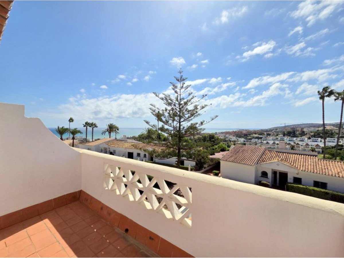 A sunny balcony overlooking the sea with palm trees and rooftops in the distance.