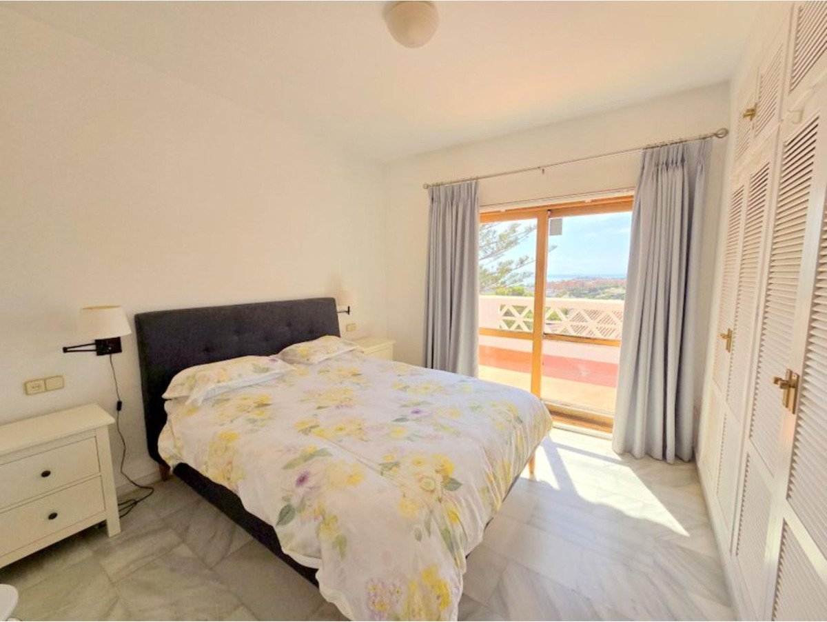 A bedroom with a bed, large windows, balcony with a sea view, and a built-in closet.