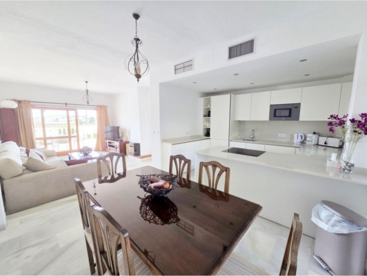 Spacious open-plan living area with dining table, sofa, and modern kitchen with white cabinets and a countertop island.
