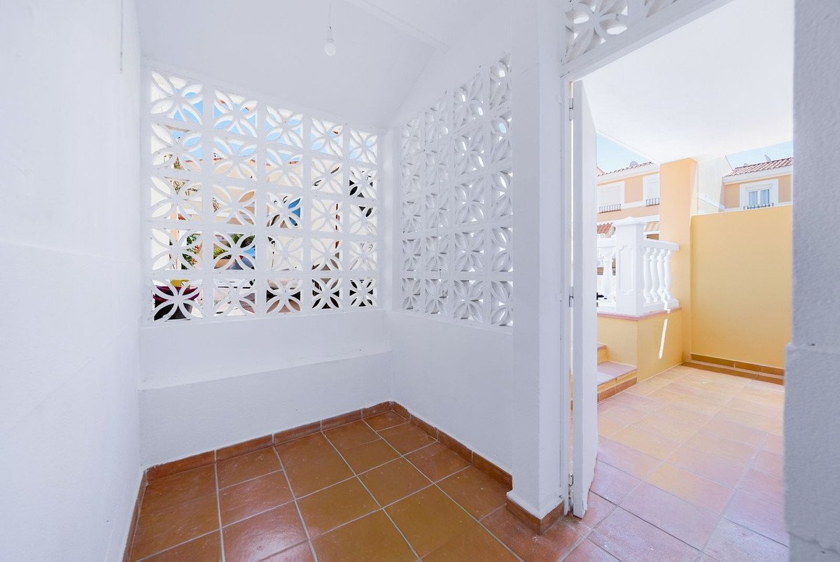 A sunlit terrace with decorative screens and terracotta flooring, offering a view of nearby buildings and a white railing.