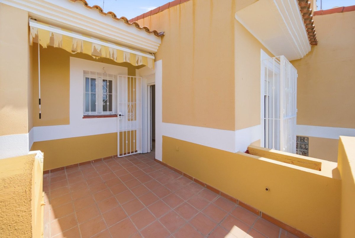 A sunny terrace with terracotta tiles, a white door with security bars, and a retractable awning over a window.