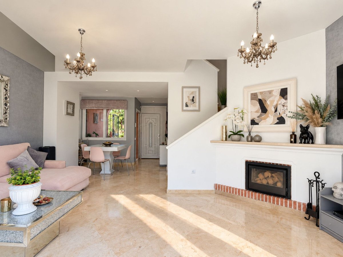 A bright living and dining area with a fireplace, a pink sofa, chandelier lighting, and a view through to a dining table.