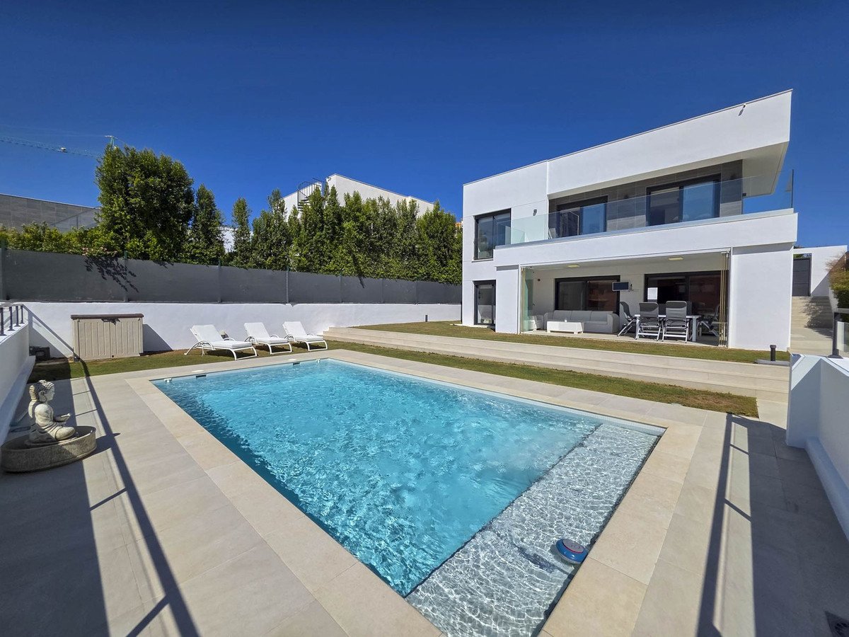 A modern white villa with a swimming pool, terrace with outdoor furniture, and sun loungers on a sunny day.