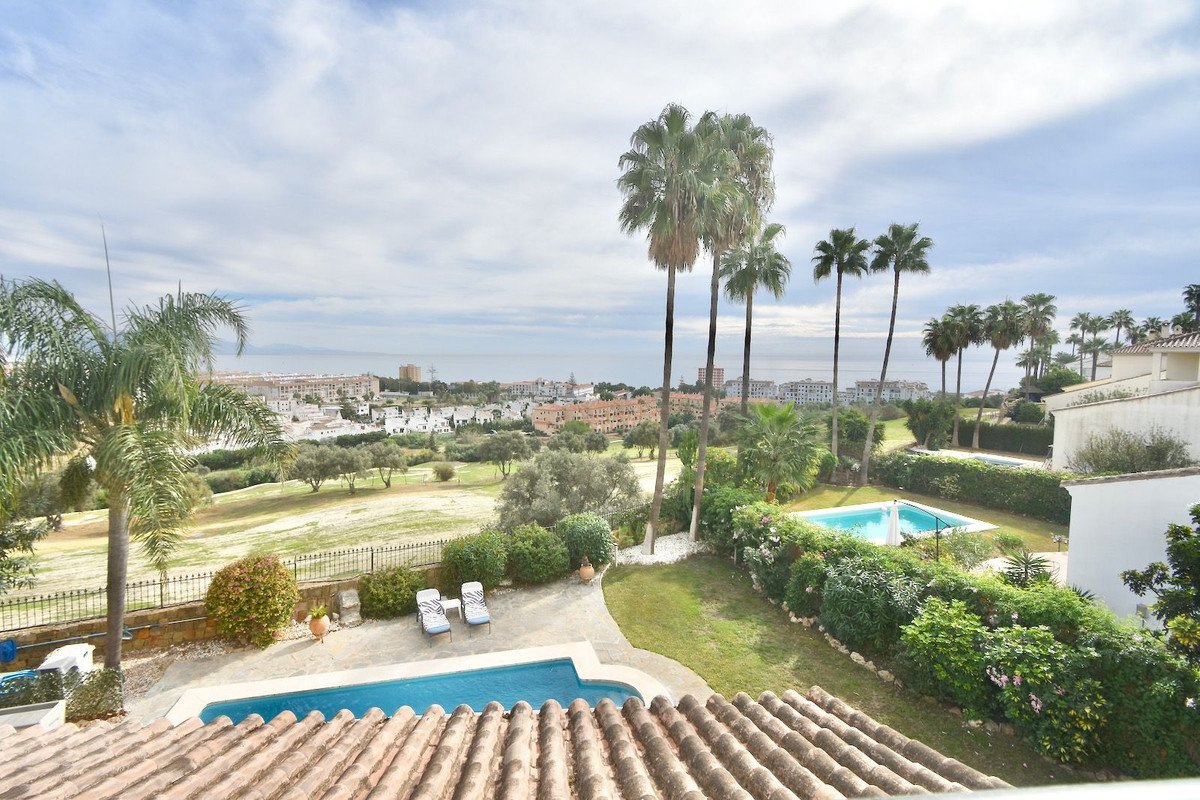 A view of a villa with two swimming pools, palm trees, and a distant view of the sea and town.