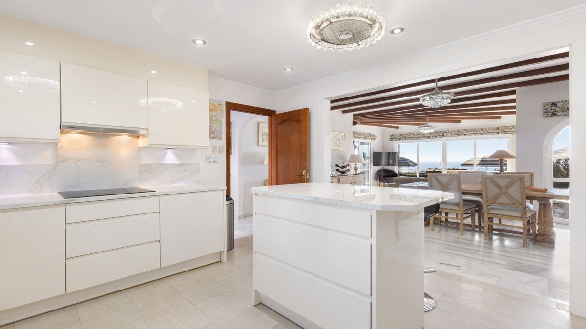 Modern white kitchen island, dining area, and living room with stunning sea views through large windows.