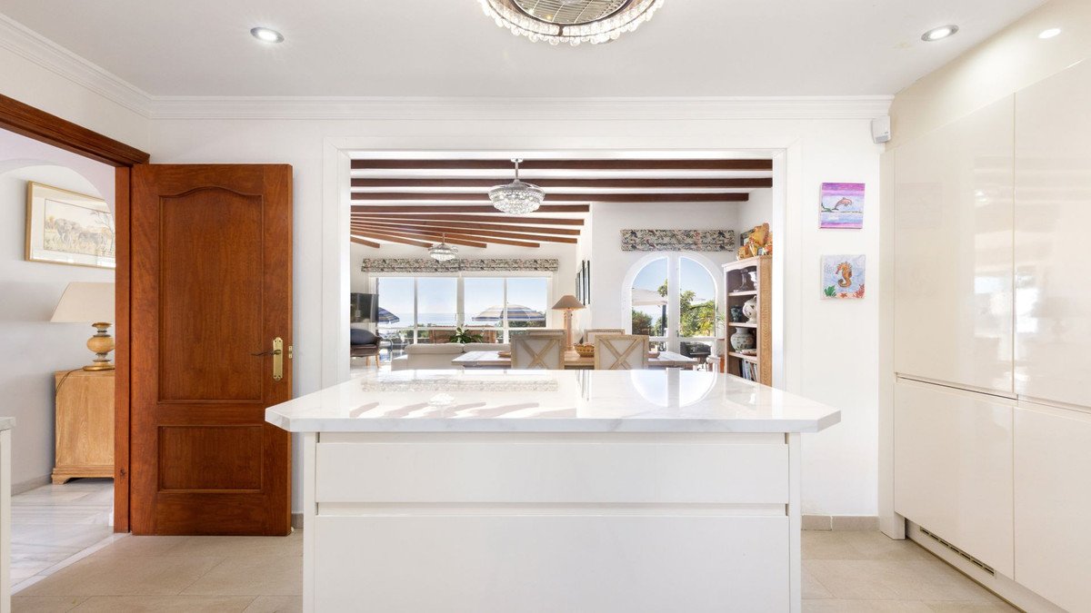 Modern kitchen island with a marble countertop and a view through to a living area with a terrace and sea view.