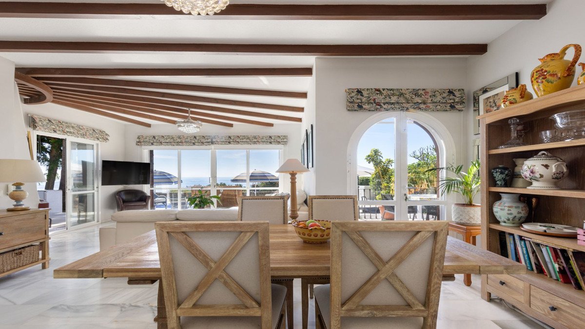 Dining area and living room with sea view, beamed ceiling, and access to terrace. Rustic wooden furniture and decor.