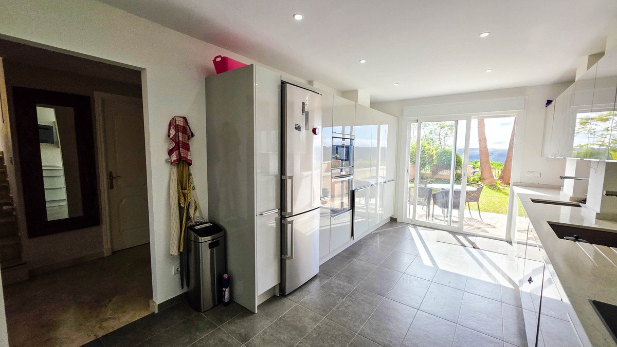Modern white kitchen with stainless steel appliances and sliding glass doors opening to a patio with an ocean view.
