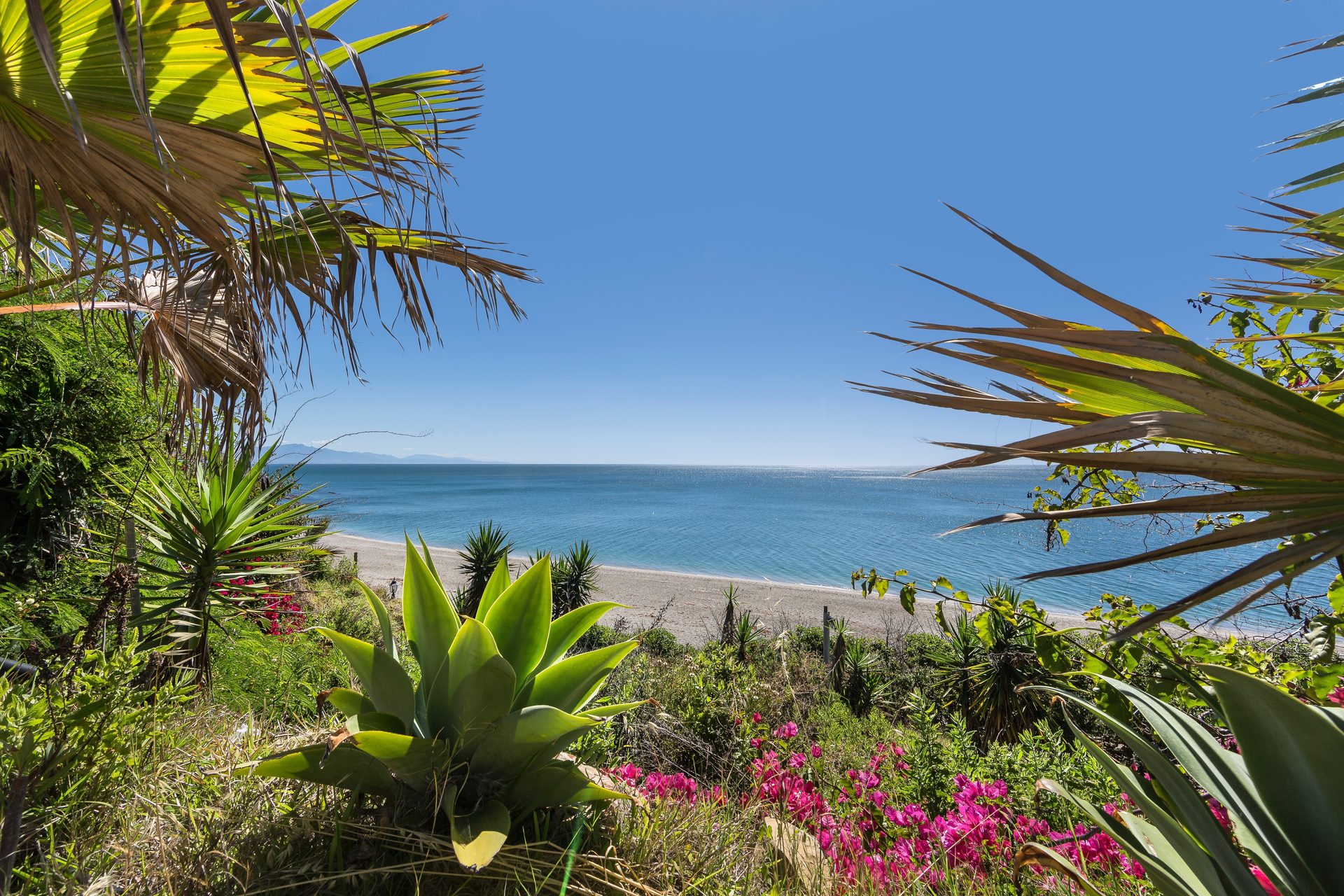 Oceanfront villa with private beach, lush garden, and stunning blue sky view.