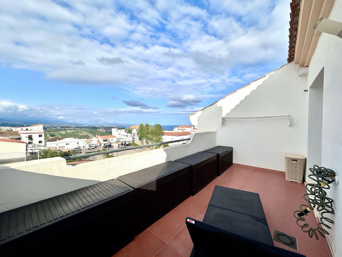 Balcony with black lounge furniture, tiled floor, and panoramic view of coastal town and sea under cloudy sky.