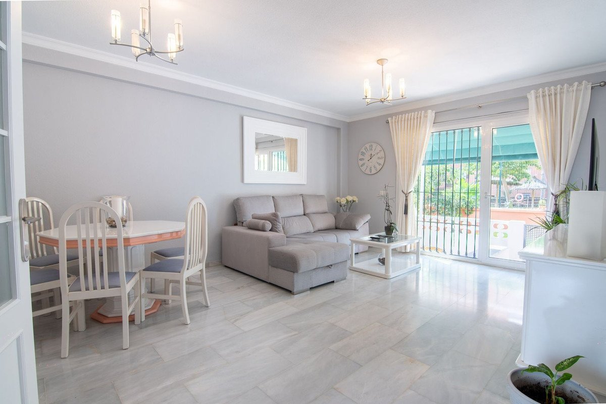 Spacious living and dining area with modern furniture, large windows leading to a patio with greenery.