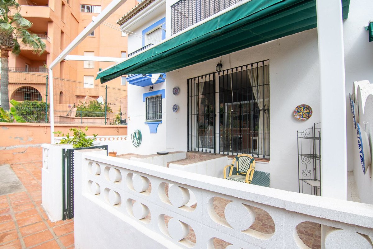 View of a white terrace with a green awning, metal security bars on windows, and outdoor seating with a view of building background buildings.