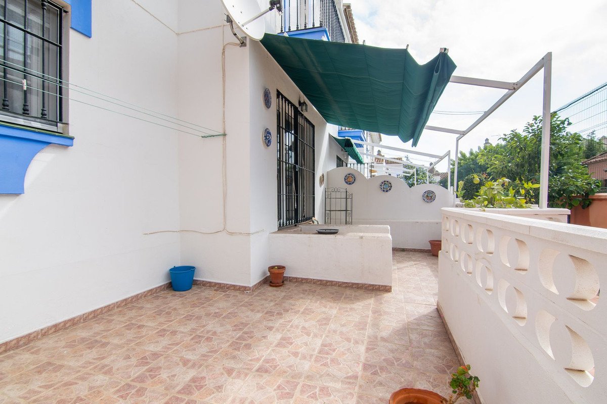 A tiled terrace with a green awning, decorative wall features, potted plants, and views of trees and sky.