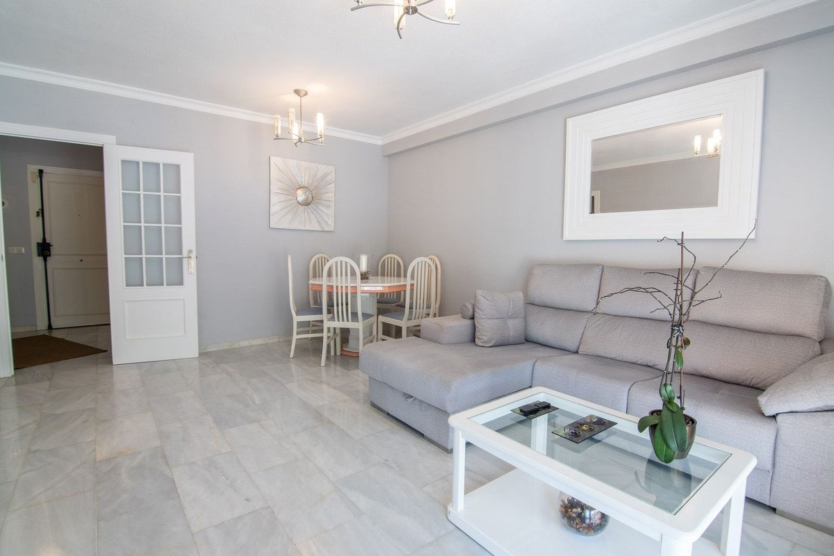 Modern living and dining area with a grey sectional sofa, glass coffee table, and dining set, featuring marble floors.