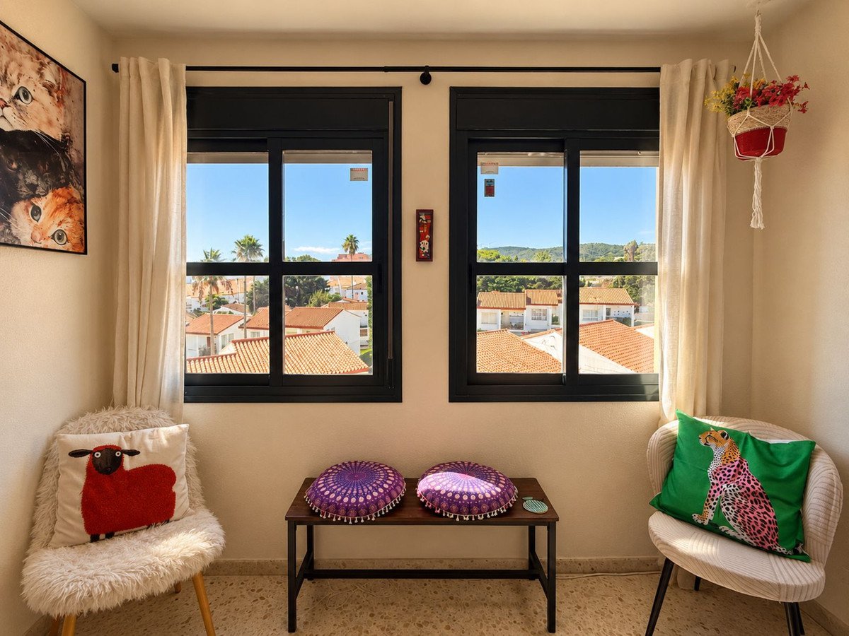 Cozy living room nook with two chairs, decorative pillows, and a view of rooftops and hills through the windows.