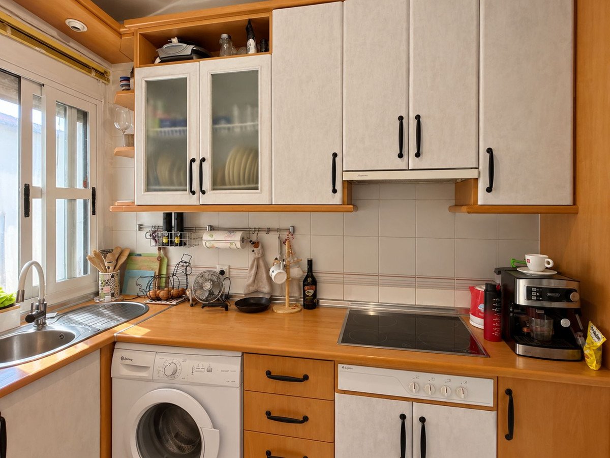 A compact modern kitchen featuring white cabinets, wooden countertops, a sink, stove, coffee maker, and a washing machine.