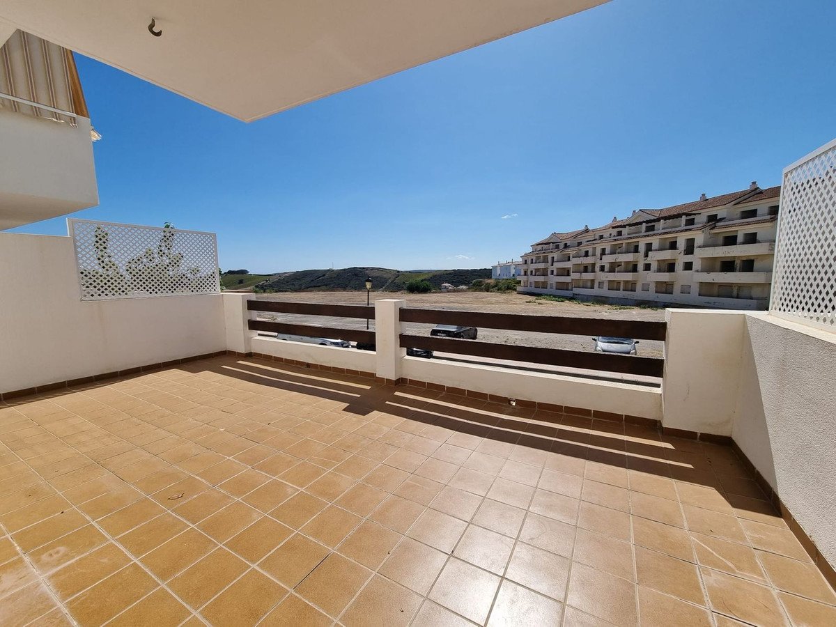 A spacious tiled terrace with a railing and a view of a large apartment building under a clear blue sky.