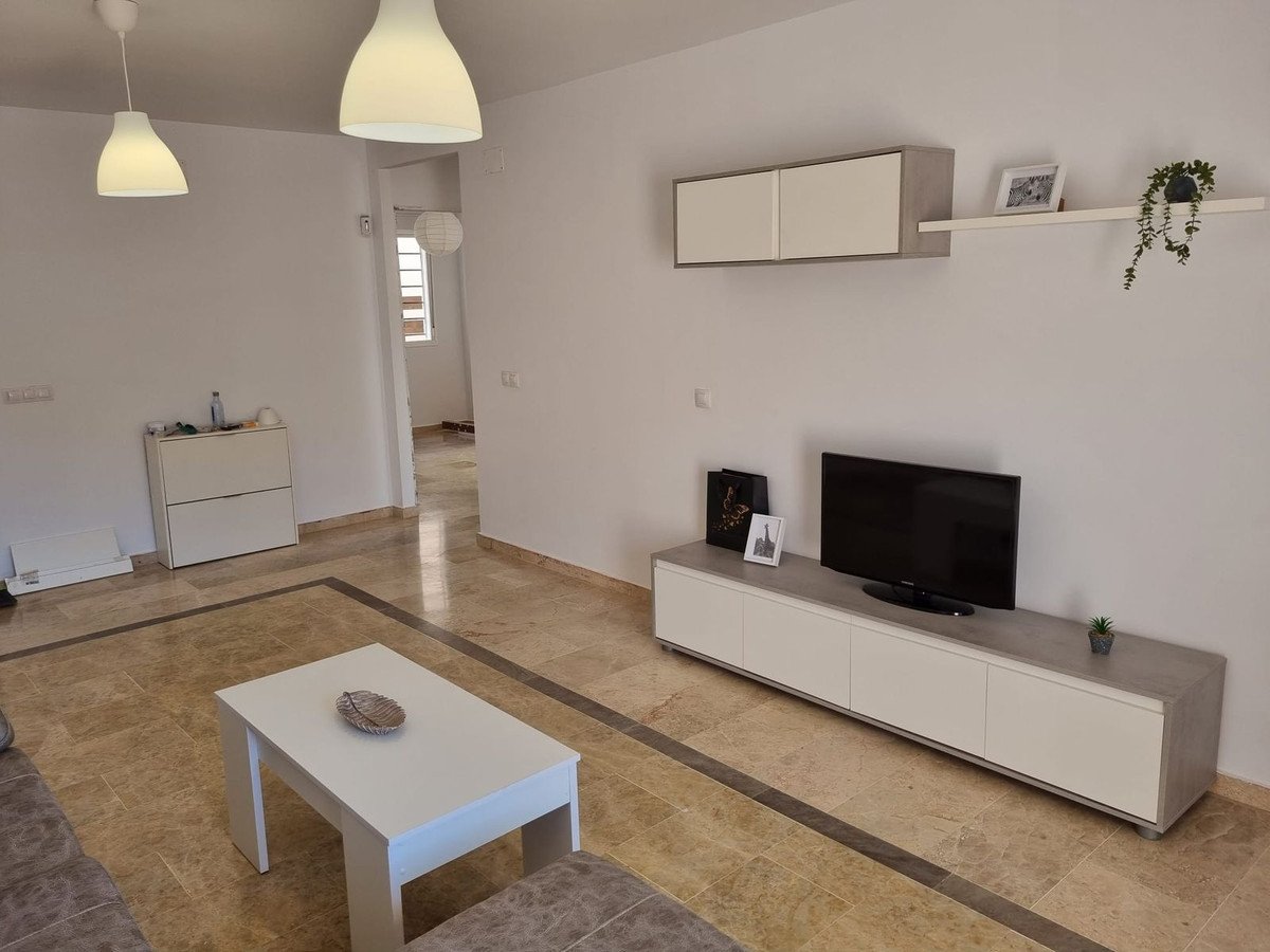 Modern living room with a TV, entertainment unit, coffee table, and bright overhead lighting. White walls and marble floors.