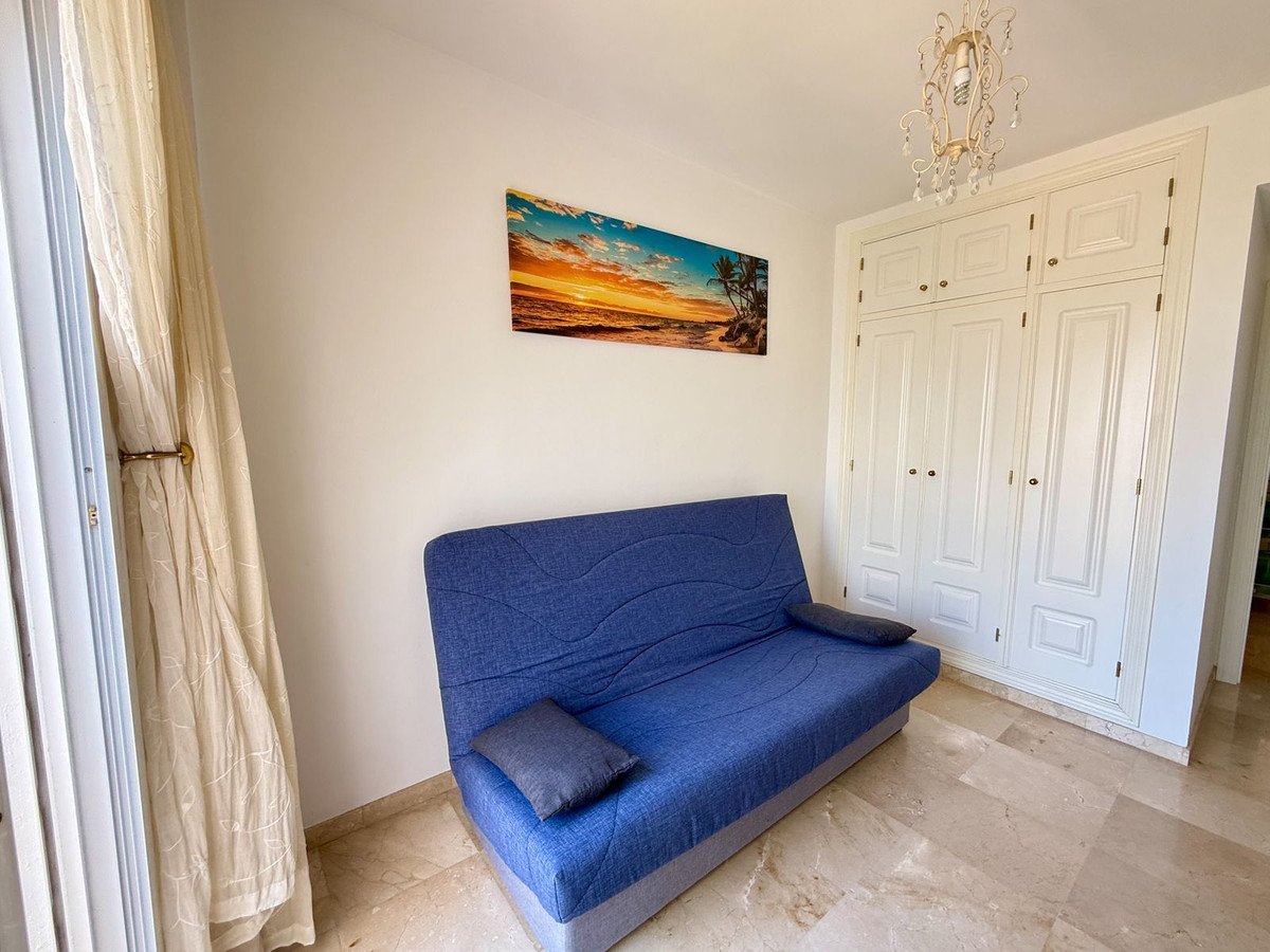Blaues Schlafsofa im hellen Zimmer mit weißen Wänden, Marmorboden, Strandbild.