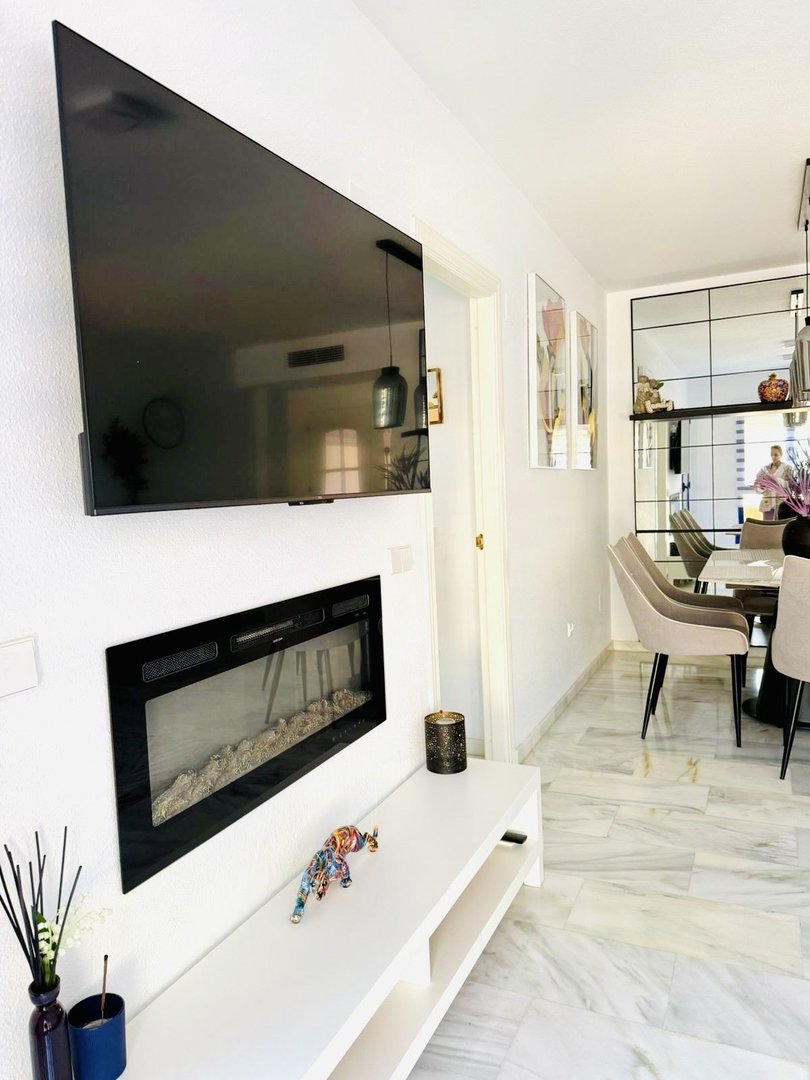 Modern living room featuring a large flat-screen TV mounted above a sleek fireplace, with a dining area in the background