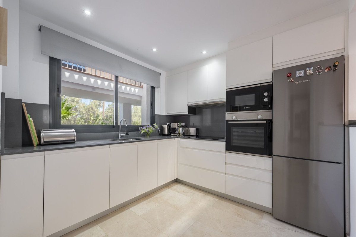 Modern kitchen with white cabinets, stainless steel appliances, and a view of greenery through a large window.