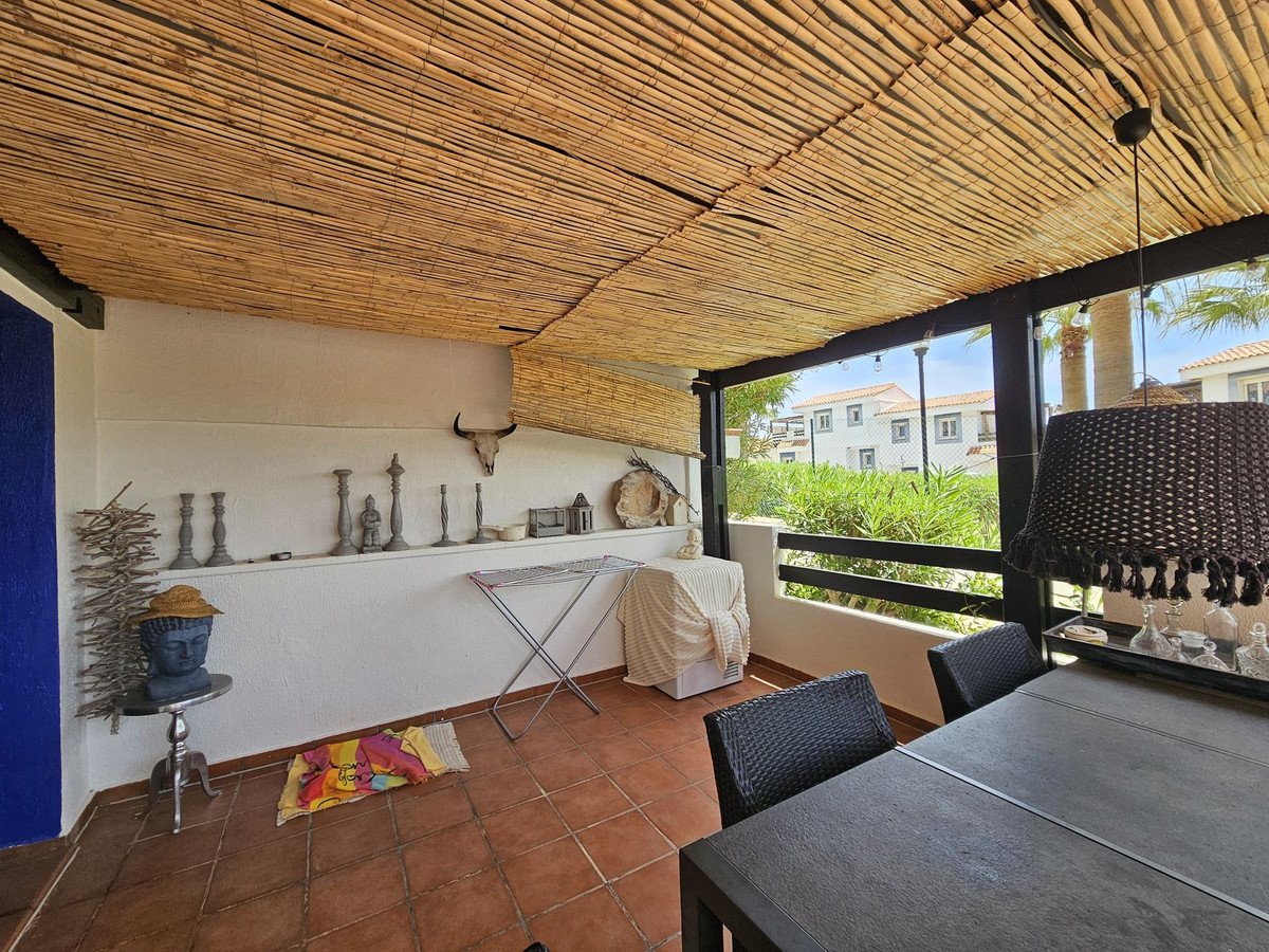 Covered patio with thatched roof, tiled floor, and outdoor dining area overlooking greenery and buildings.