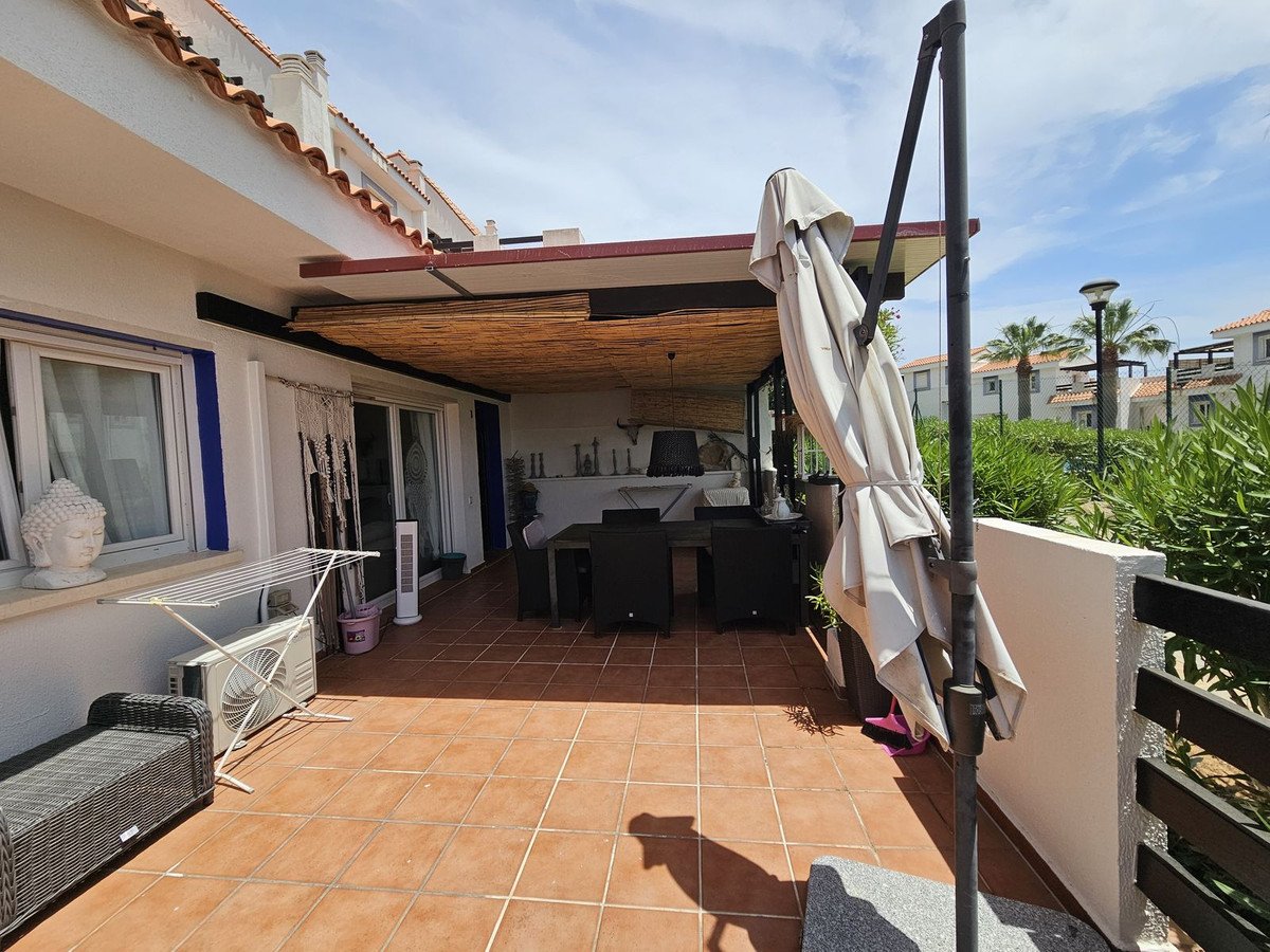 Covered patio with tiled floor, outdoor dining set, and umbrella, overlooking greenery and neighboring buildings.
