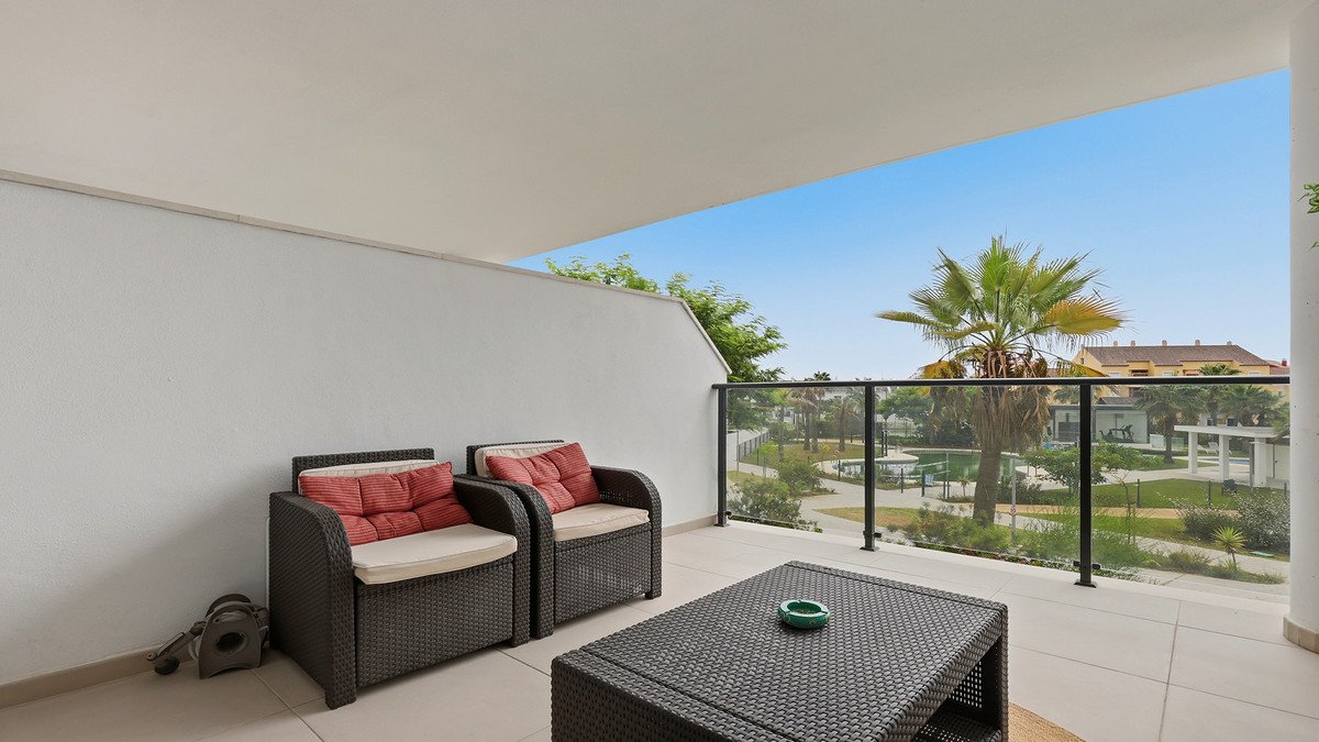 A furnished terrace with seating and a coffee table, offering a view of palm trees and a garden area under a clear blue sky.