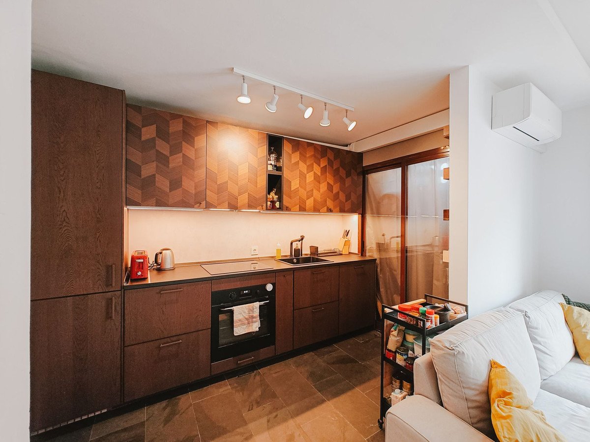 Moderne keuken met houten kasten, witte sofa en spotverlichting.