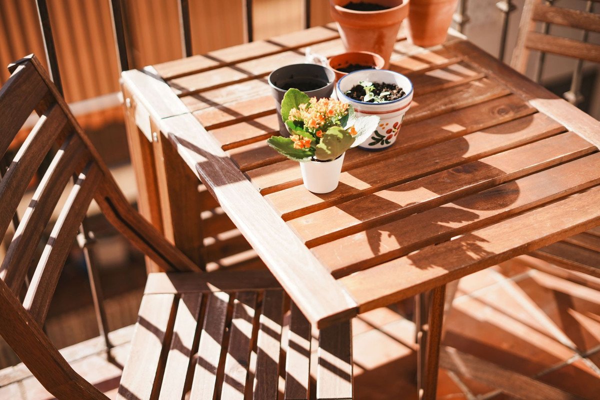 Houten balkon tafel met planten en stoelen, zonnig zitje buiten.
