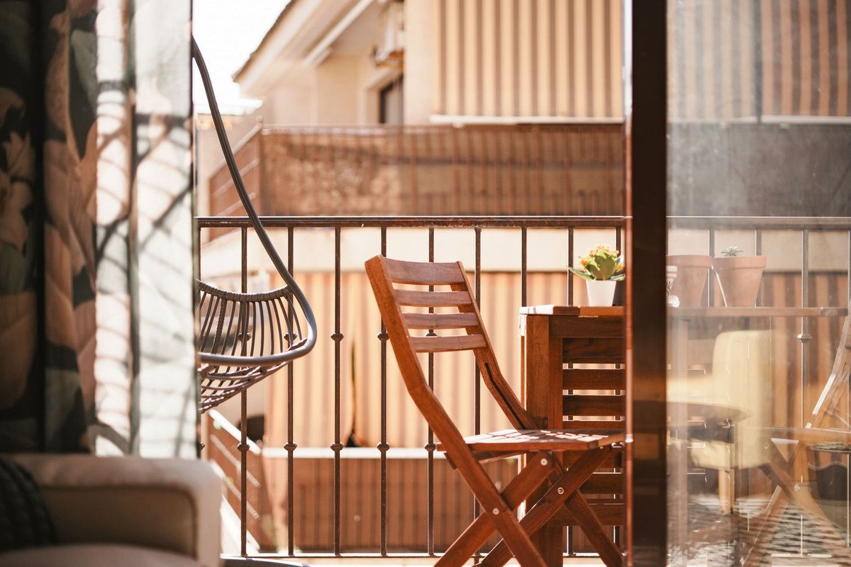 Balkon met houten tafel, stoel en hangende rotan stoel.