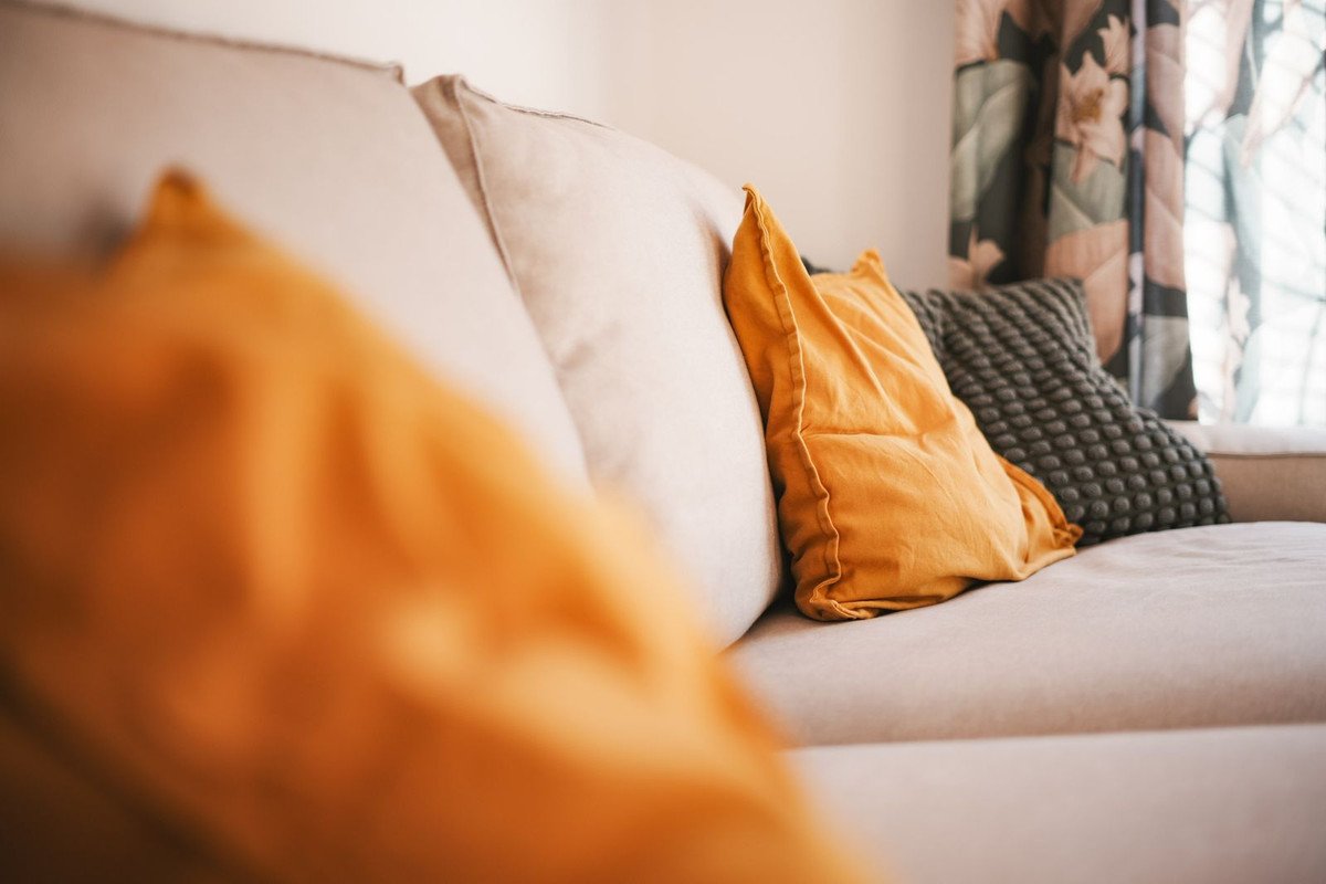 Beige sofa met kussens, bloemen gordijnen en natuurlijk licht.