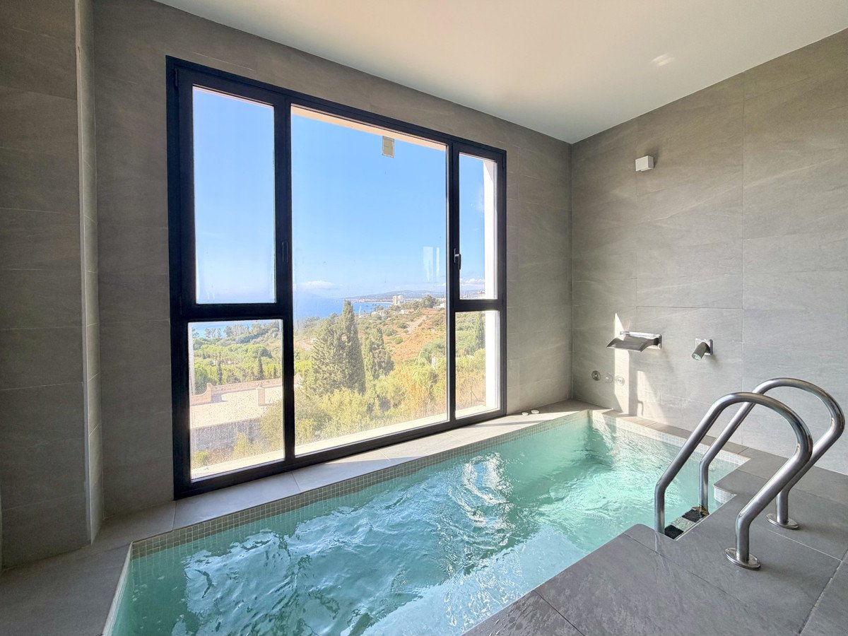 Modern indoor plunge pool with steps and ladders, featuring large windows with stunning sea and landscape views.