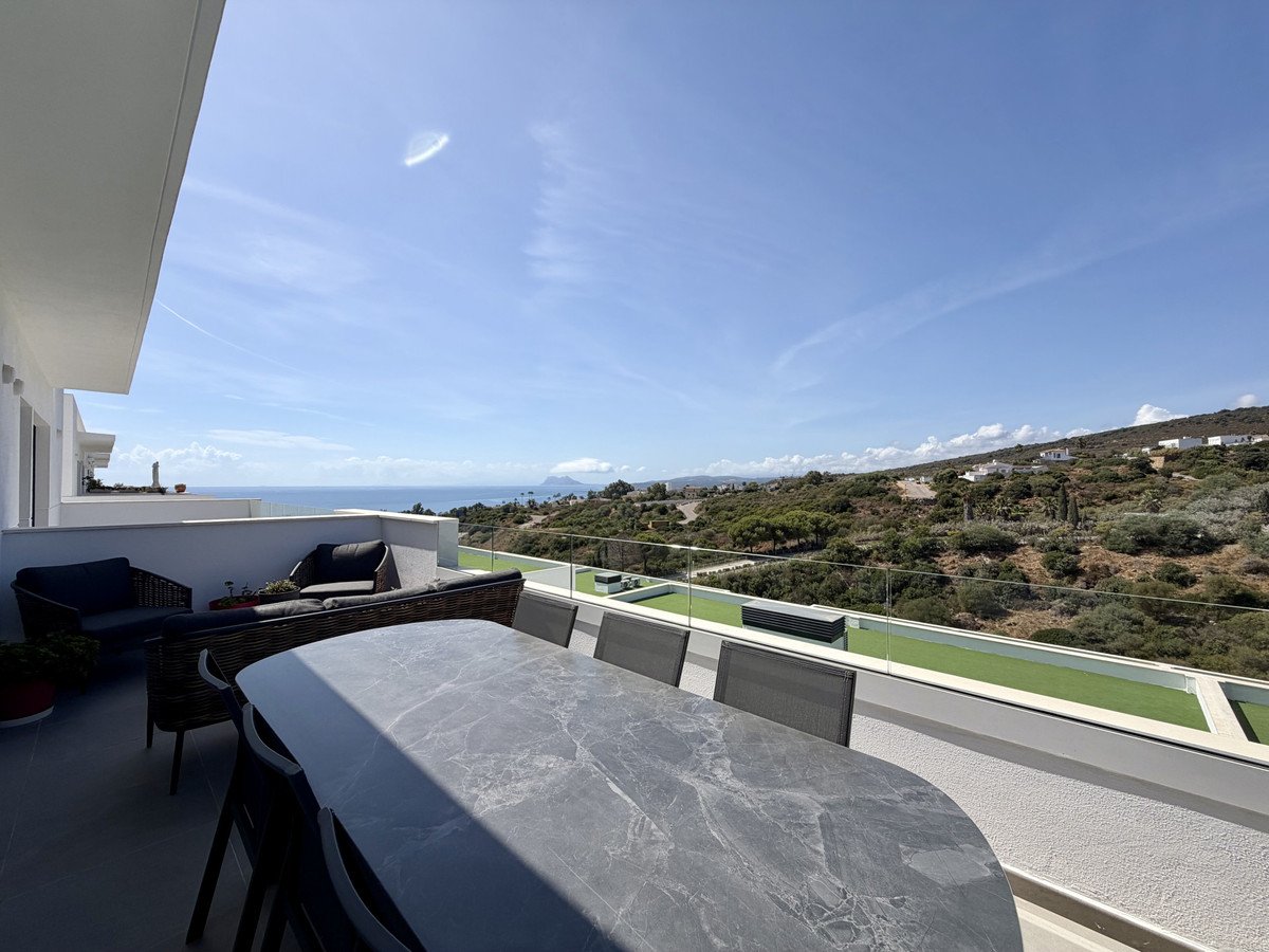 Spacious terrace with dining table, seating area, and stunning sea and hill views under a clear blue sky.