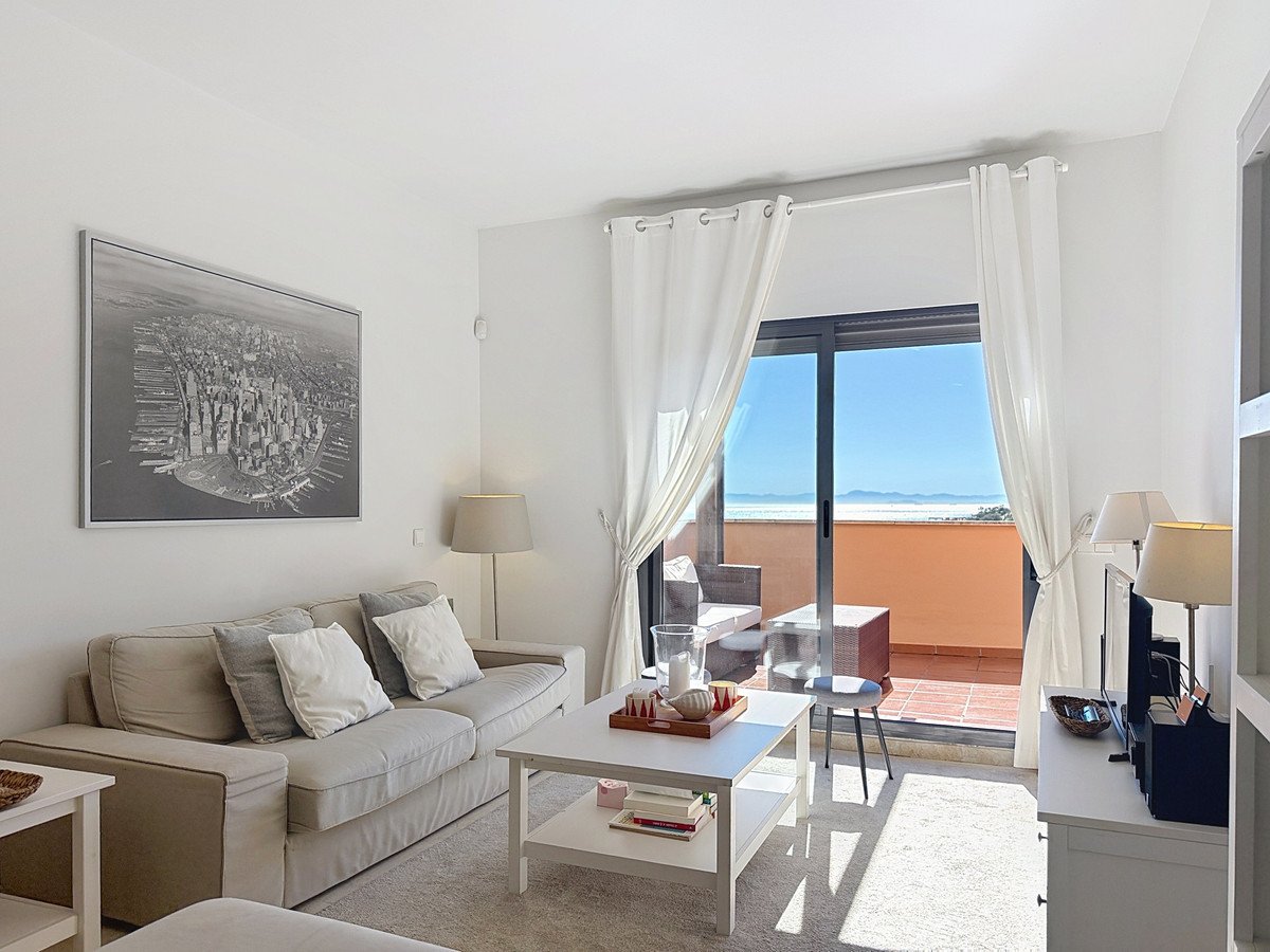 Bright living room with sofa, coffee table, and large sliding doors opening to a balcony with a sea view.