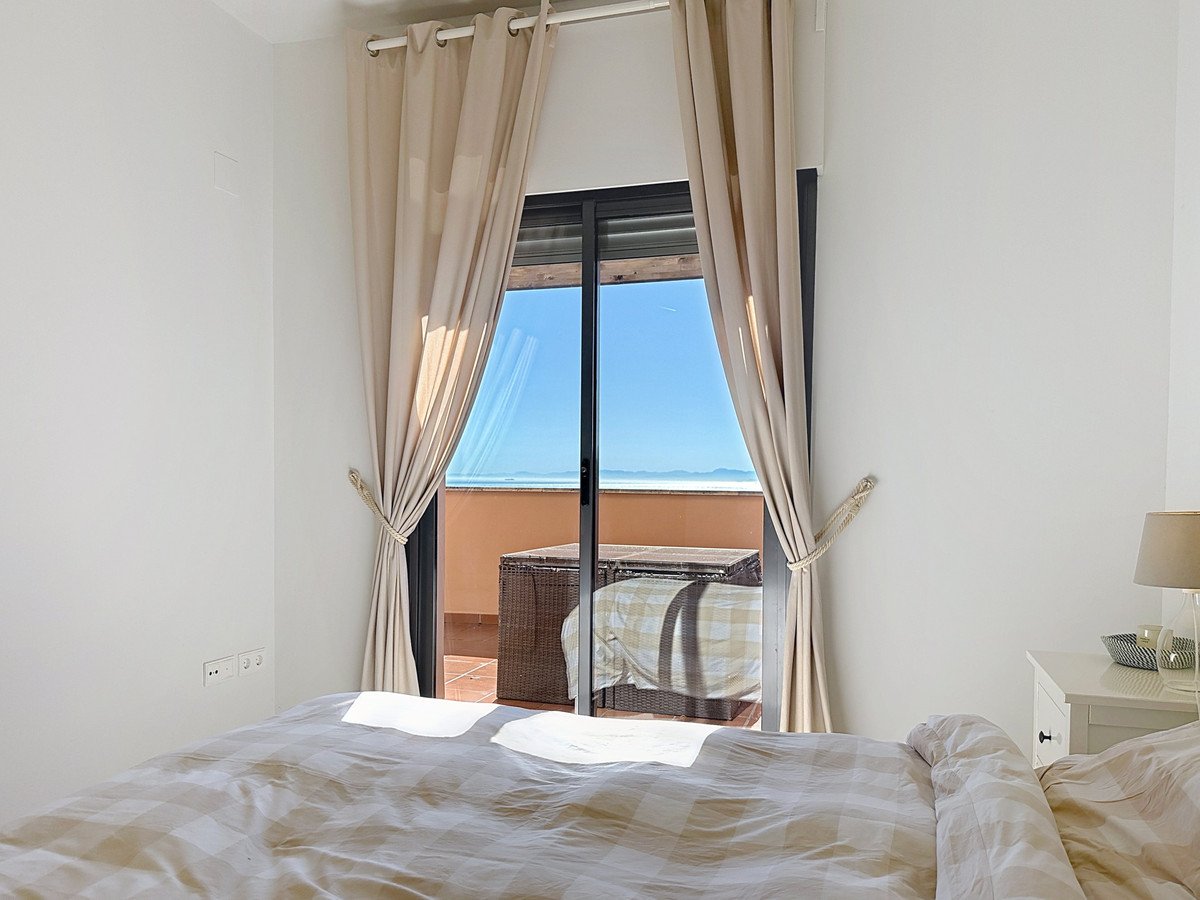 Bedroom with a bed, curtains open to a balcony with outdoor furniture and a distant sea view.