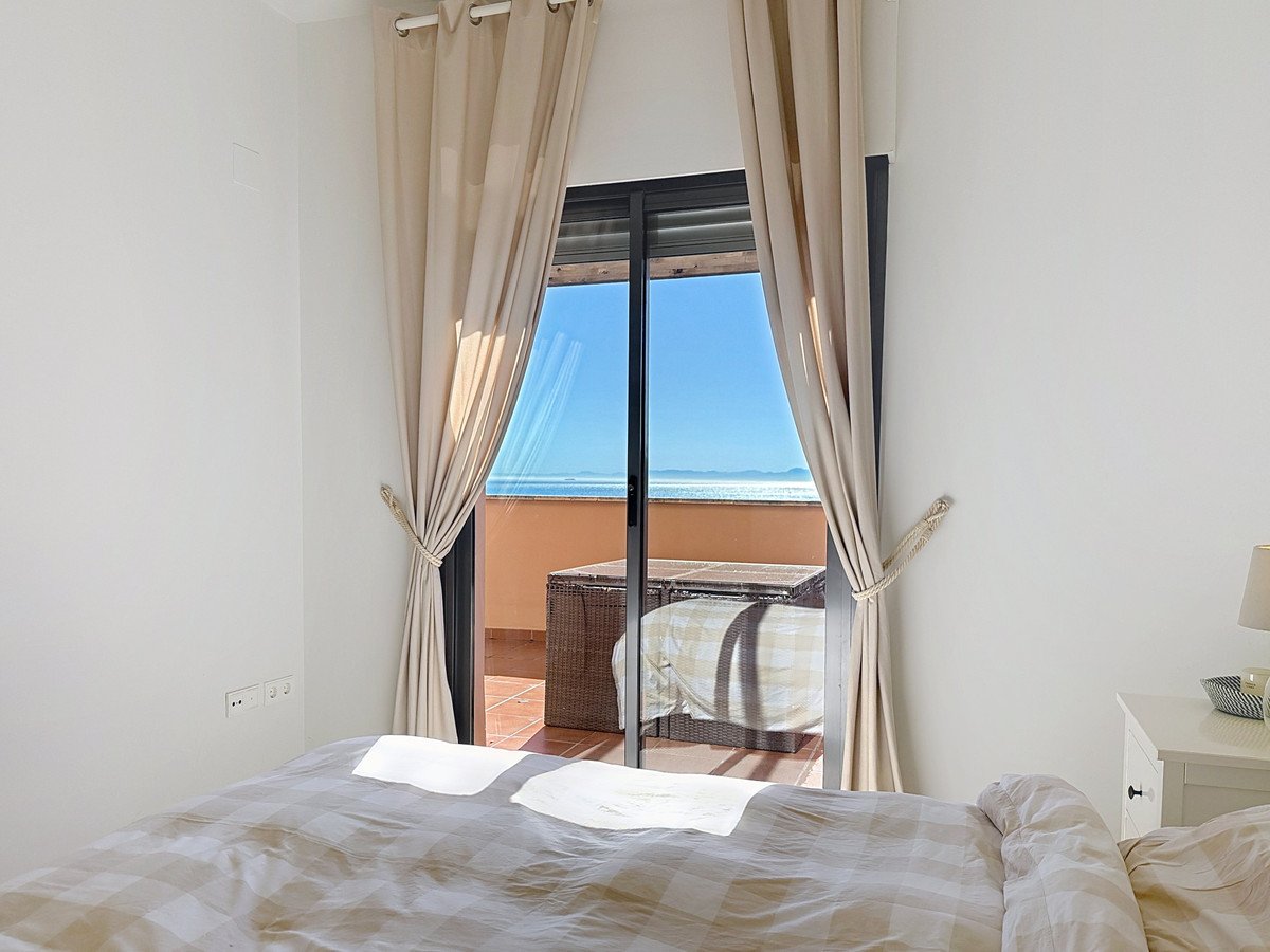 Bedroom with beige curtains opening to a balcony with sea view and outdoor seating.
