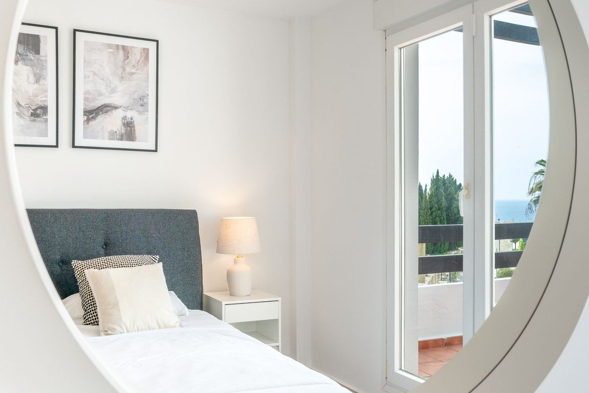Bedroom with a bed, a bedside table with a lamp, and a door leading to a balcony with a sea view.